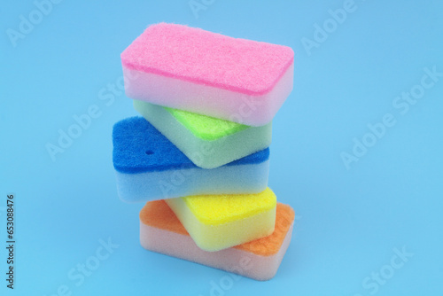 Stack of different colored new sponges on blue background. Copy space for text.