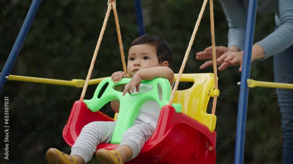 mother with infant baby is playing in a swing in the garden mother with infant baby is playing in a swing in the garden