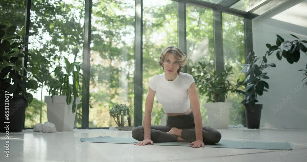 young caucasian fitness woman practicing yoga on a yoga mat in a modern studio with plants and large forest or garden overlooking windows young caucasian fitness woman practicing yoga on a yoga mat in a modern studio with plants and large forest or garden overlooking windows