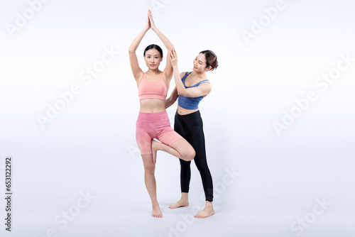 Asian woman in sportswear doing yoga exercise in standing pose with her trainer or yoga buddy. Healthy body care and meditation yoga lifestyle in full shot on isolated background. Vigorous