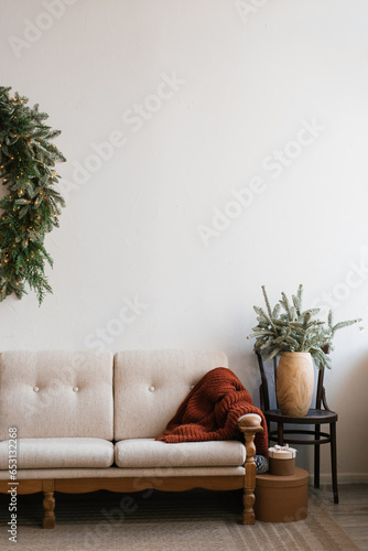 Stylish Christmas tree in a pot stands near a white sofa with pillows in the living room of the house
