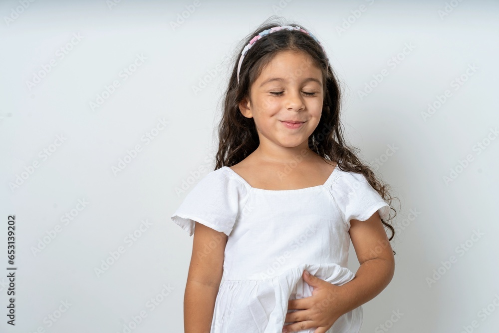 beautiful kid girl wearing white dress touches tummy, smiles gently, eating and satisfaction concept. beautiful kid girl wearing white dress touches tummy, smiles gently, eating and satisfaction concept.