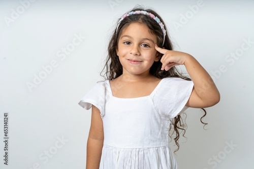 Photos beautiful kid girl wearing dress tries to memorize something, keeps fore finger