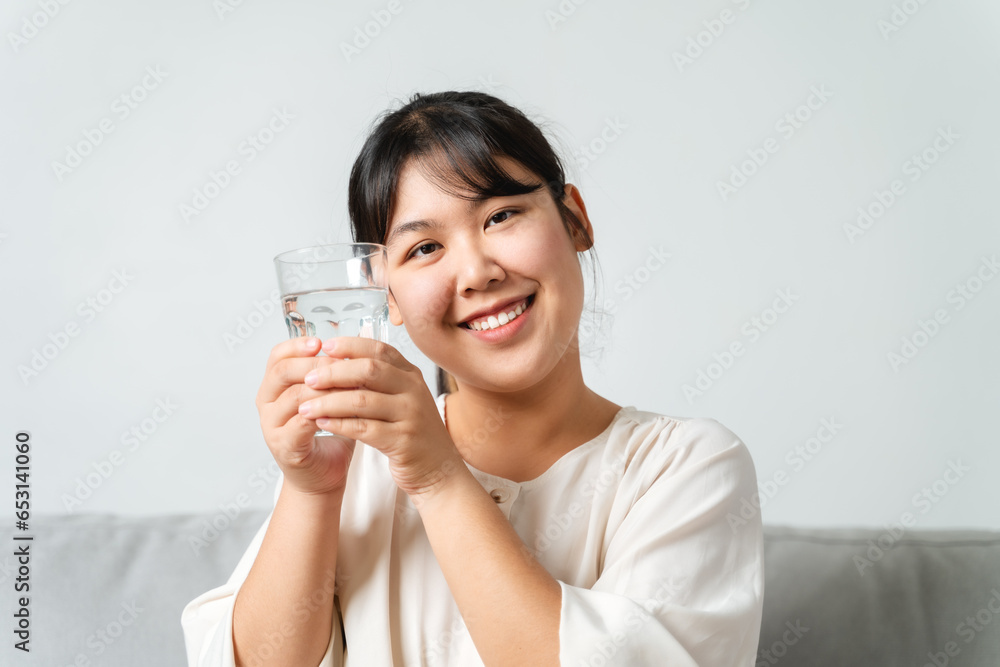 healthy beautiful young woman holding a glass of water sitting on the couch at the livingroom. healthy beautiful young woman holding a glass of water sitting on the couch at the livingroom.