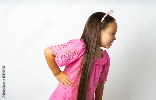 beautiful kid girl wearing pink dress Suffering of backache, touching back with hand, muscular pain