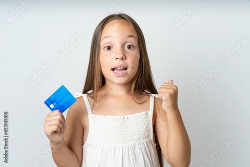 Photo of lucky impressed beautiful kid girl wearing white dress arm fist holding credit card. Celebrated © Roquillo
