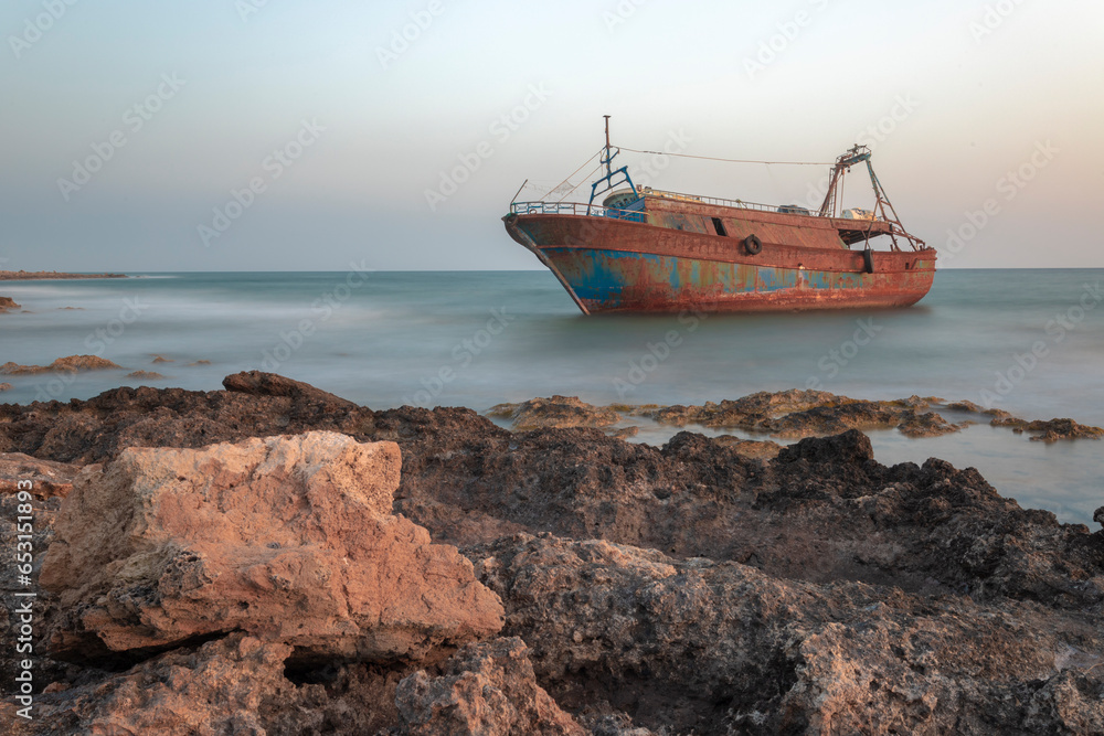 Fototapeta premium Rusty shipwreck on rocky beach with sky and ocean.