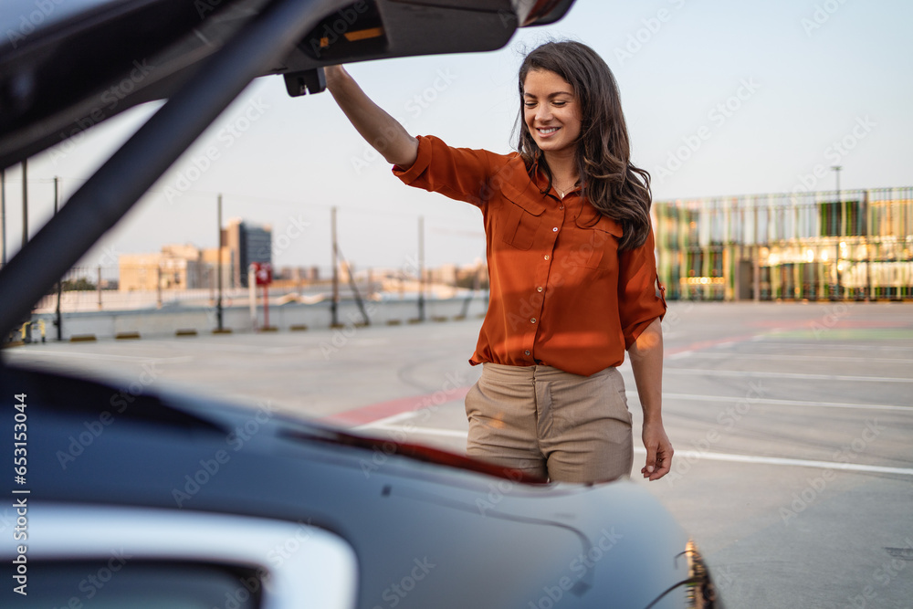 Obraz premium Woman closing car trunk parked. One woman Caucasian female standing by the back trunk of her car on the parking lot