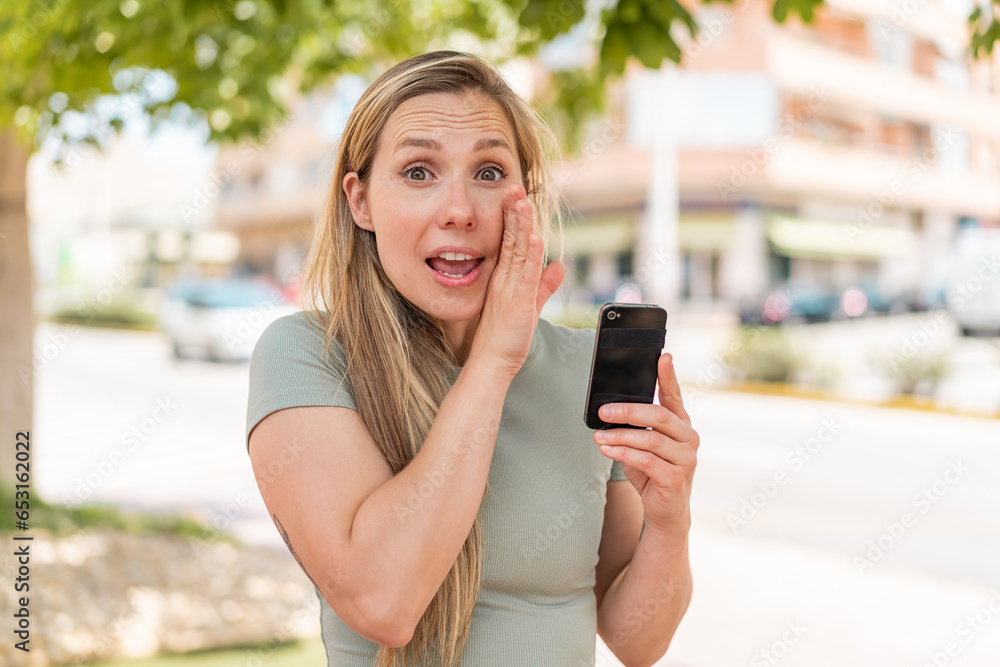 Young blonde woman using mobile phone at outdoors whispering something Young blonde woman using mobile phone at outdoors whispering something