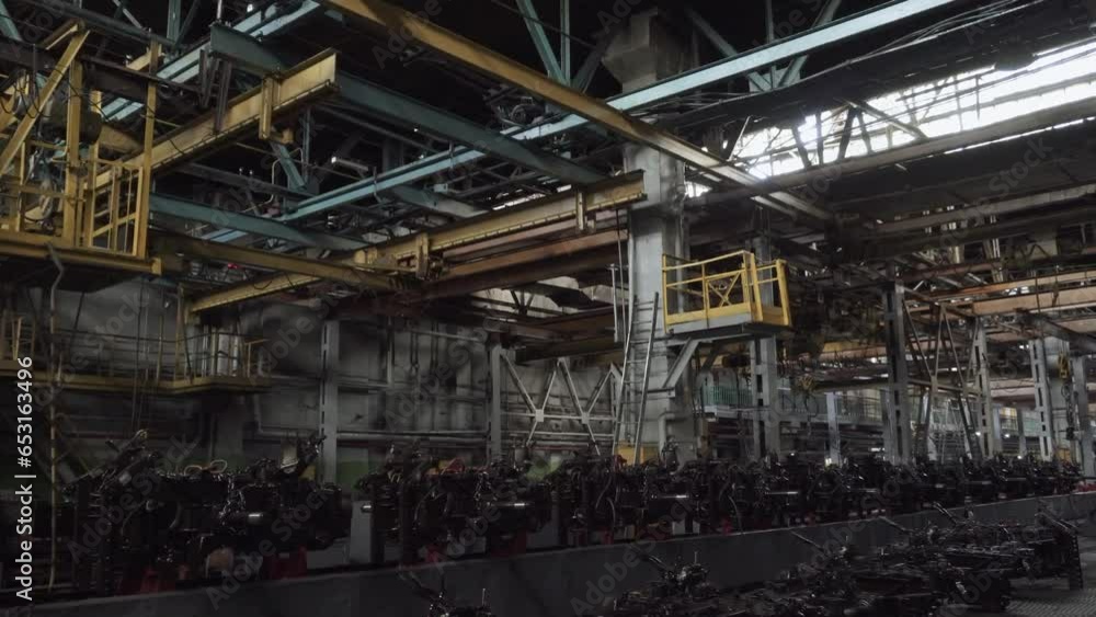Dark assembly factory floor with automotive components and lifting mechanisms. Closed bankrupt factory without people. System of lifting mechanisms with powerful multi-ton hoists on beams. Dark assembly factory floor with automotive components and lifting mechanisms. Closed bankrupt factory without people. System of lifting mechanisms with powerful multi-ton hoists on beams.