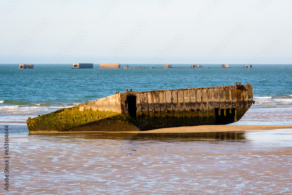 An element of the former Mulberry harbor built on Gold Beach in Arromanches, Normandy, in WWII, lying on the sand at low tide with remains of Phoenix caissons in the distance.