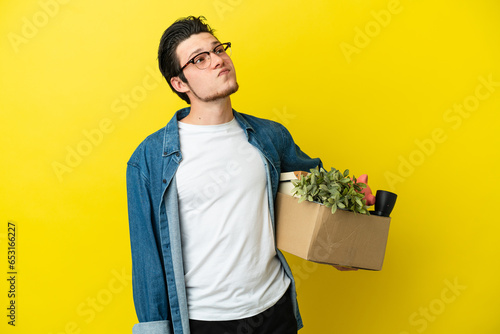 Russian Man making a move while picking up a box full of things isolated on yellow background and looking up