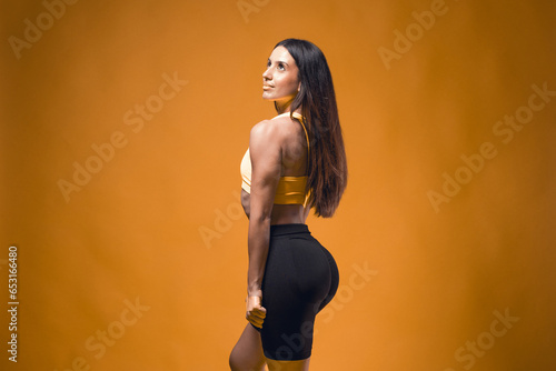 Young sportive attractive caucasian athlete woman posing in yellow tank top and black sauna shorts fitness outfit. Studio shooting of pretty slim fit brunette doing aerobic stretching with rubberbands photo