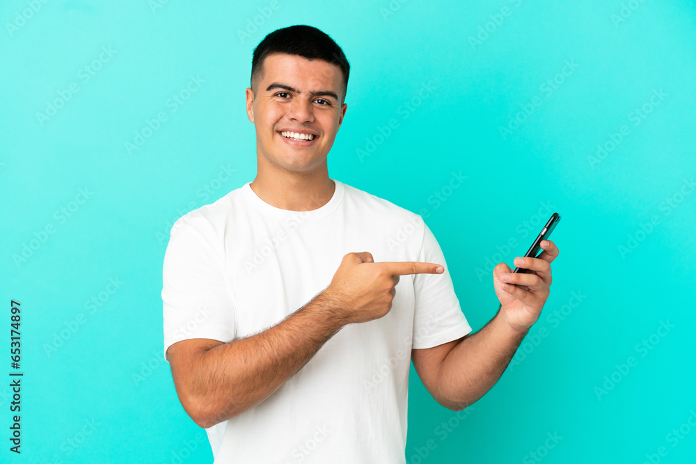 Young handsome man over isolated blue background using mobile phone and pointing it Young handsome man over isolated blue background using mobile phone and pointing it