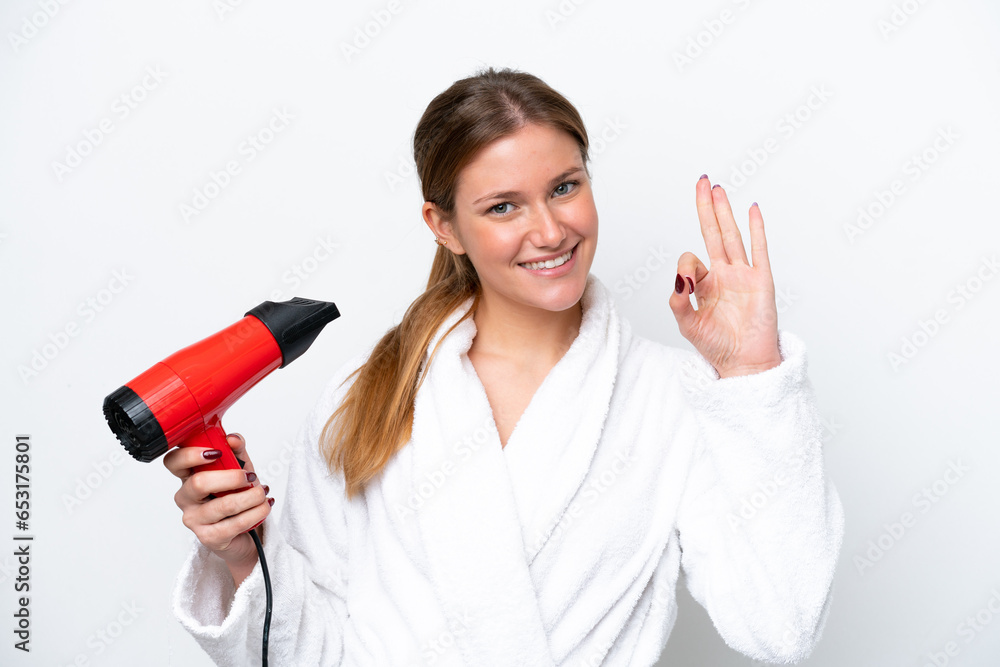 Young caucasian woman holding hairdryer isolated on white background showing ok sign with fingers Young caucasian woman holding hairdryer isolated on white background showing ok sign with fingers