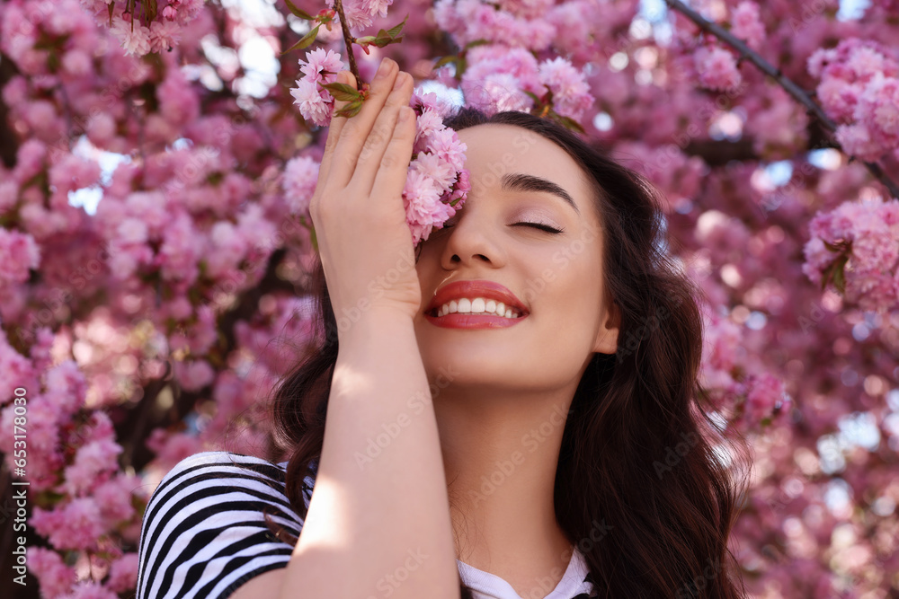 Fototapeta premium Beautiful woman near blossoming sakura tree on spring day