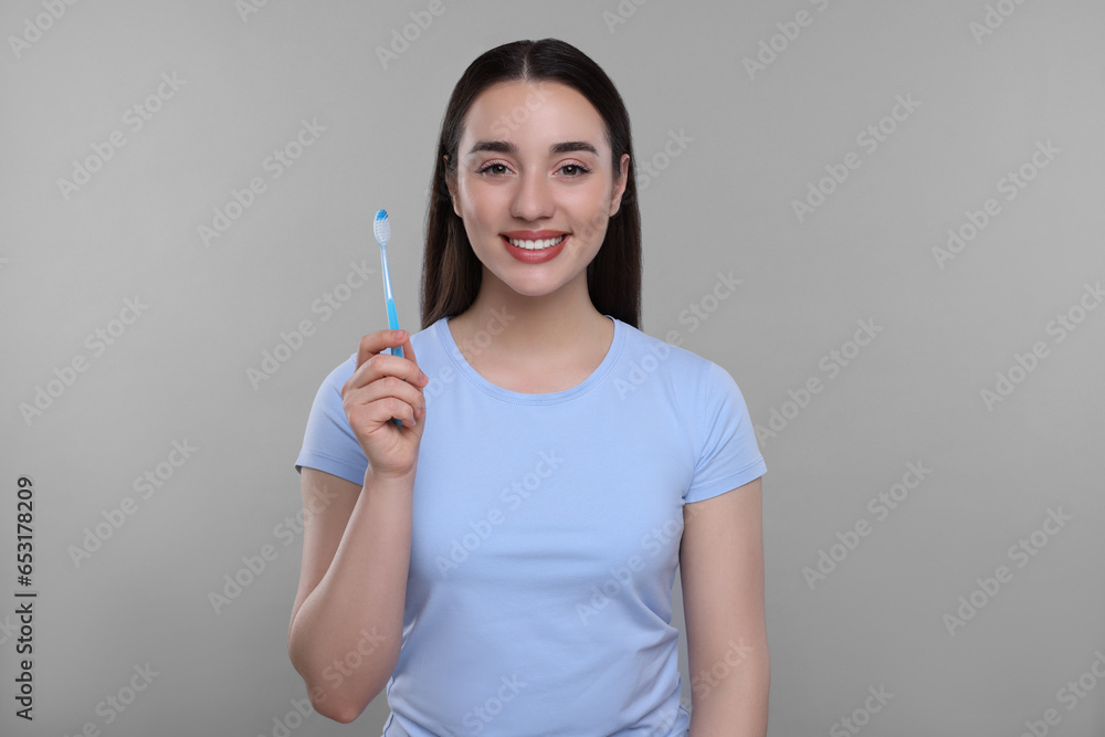 Happy young woman holding plastic toothbrush on light grey background Happy young woman holding plastic toothbrush on light grey background
