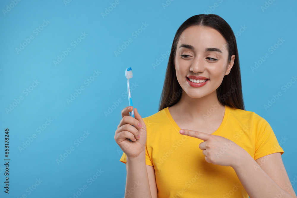 Happy young woman holding plastic toothbrush on light blue background, space for text Happy young woman holding plastic toothbrush on light blue background, space for text