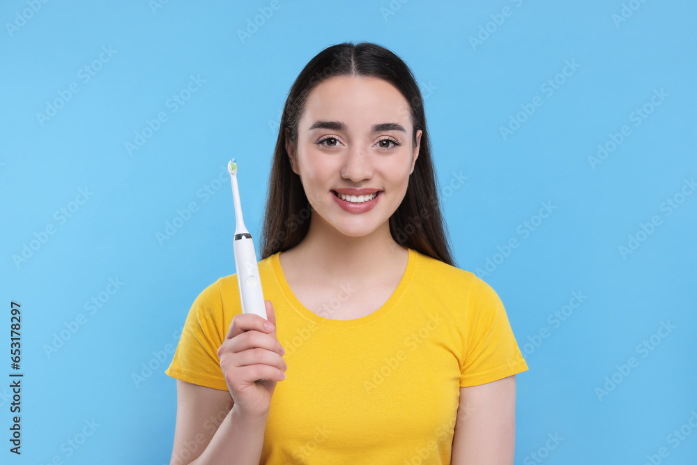 Happy young woman holding electric toothbrush on light blue background Happy young woman holding electric toothbrush on light blue background