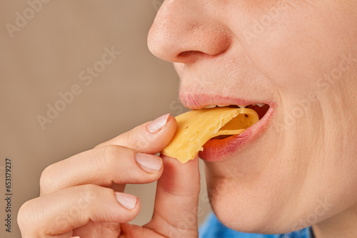 Close-up of a happy Caucasian woman holding a slice of cheese with her hand and biting it. Side view. Low angle view.