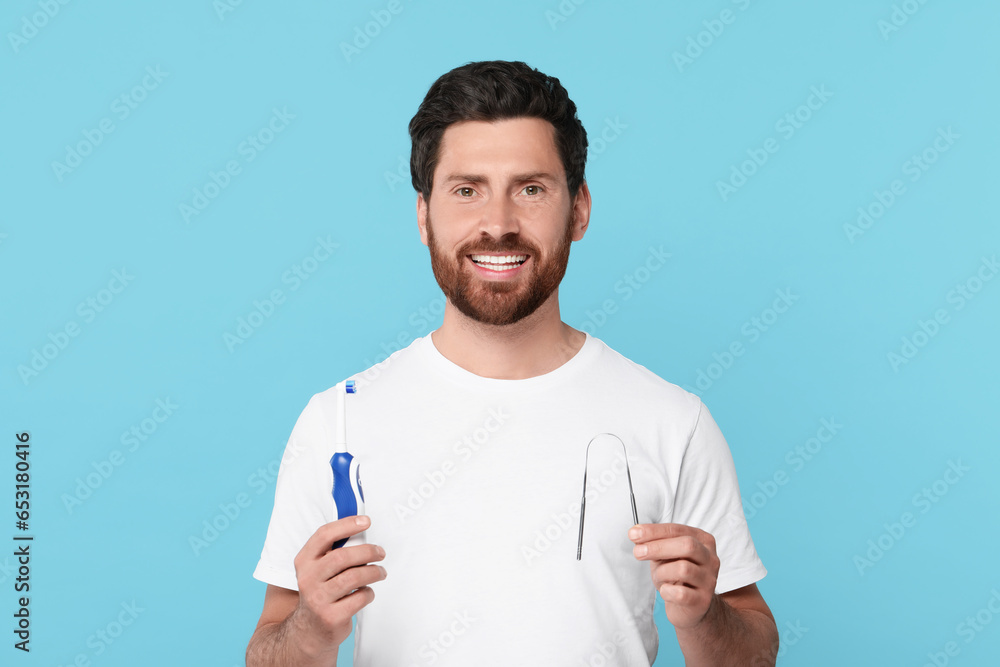 Happy man with tongue cleaner and electric toothbrush on light blue background Happy man with tongue cleaner and electric toothbrush on light blue background