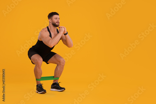 Young man exercising with elastic resistance band on orange background. Space for text © New Africa