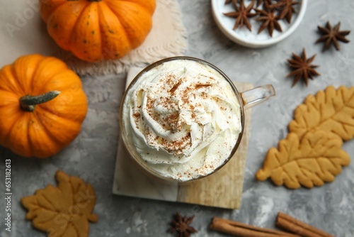Cup of pumpkin spice latte with whipped cream, cookies and ingredients on light grey table, flat lay