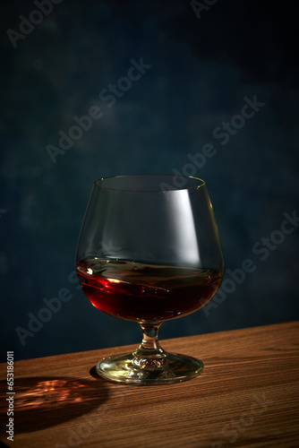 Close up photo of glass of whiskey, rum, brandy or gin with shadow standing on wooden table over dark background.