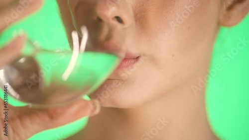 Close up shot of a young woman drinking a glass of water and enjoying the first sip and quenching her thirst with it against green background