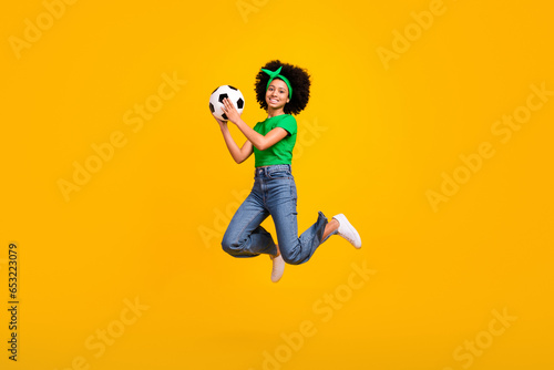 Full length photo of sportive excited teenager schoolgirl jump hands hold catch football isolated on yellow color background photo