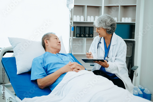  Friendly Female Head Nurse Making Rounds does Checkup on Patient Resting in Bed. She Checks tablet while Man Fully Recovering after Successful Surgery in hospital