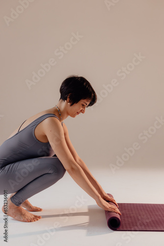 A young woman turns a mat before or after a yoga class in the studio. Close-up legs of a woman doing yoga while sitting on a light background