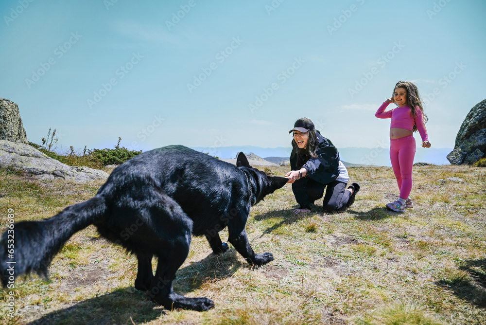 Woman and kid playing with black dog in the mountain Woman and kid playing with black dog in the mountain