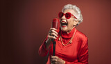 Happy old woman singing with microphone, having fun, expressing musical talent over red background