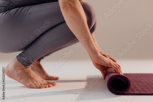 A young woman turns a mat before or after a yoga class in the studio. Close-up legs of a woman doing yoga while sitting on a light background photo