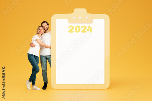Happy young european guy and woman in casual hugging near big plan with empty space