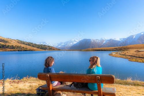 Two women sitting on a wooden bench while enjoying the nature landscape.