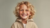 A cute little boy with golden locks showcases his infectious happiness in a softly lit beige studio.