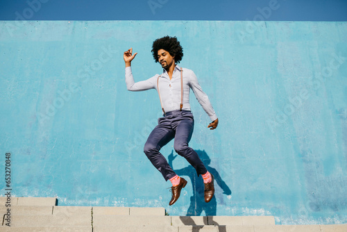 Stylish man jumping in the air in front of blue wall photo