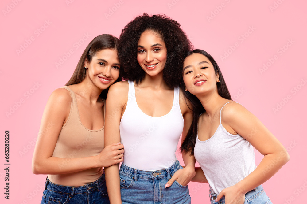 Happy young asian, black and european women posing and enjoying their natural beauty, standing on pink background Happy young asian, black and european women posing and enjoying their natural beauty, standing on pink background