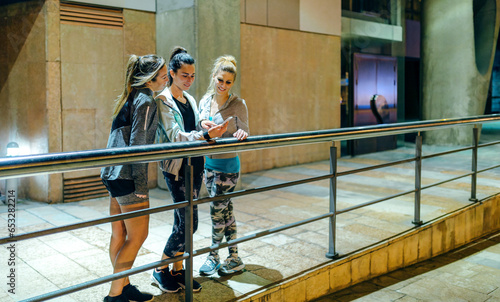Bilde på lerret Smiling sportswomen group looking cellphone while resting over banister after training at night
