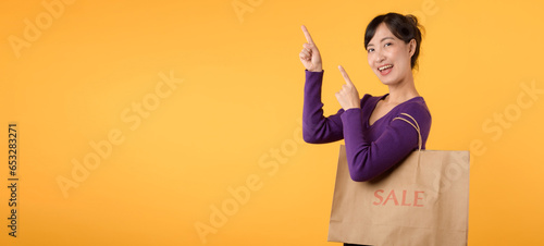 An attractive model  dressed in a purple shirt and holding a shopping bag  symbolizes the joy of a successful shopping spree in a retail store against a yellow background.