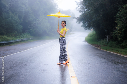 portrait of young woman standing and holding umblella in the middle of the road in the rainy season photo