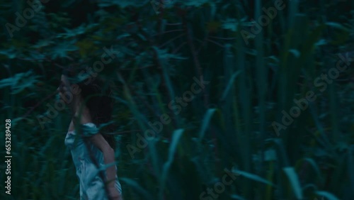 A frightened girl in a bloodstained dress runs away from her pursuer through the woods