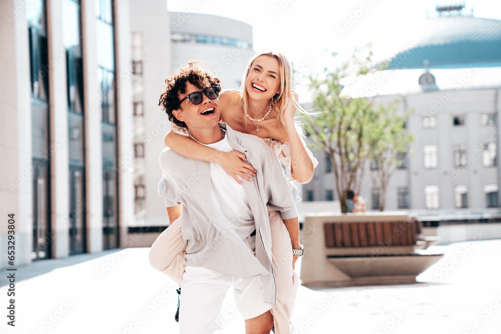 Naklejka premium Young smiling beautiful woman and her handsome boyfriend in casual summer clothes. Happy cheerful family. Couple posing in street at sunny day. Female sits at his back. piggyback riding