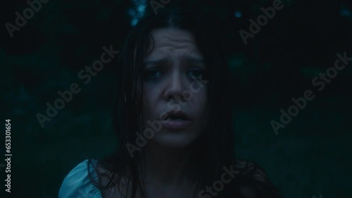 A tired, frightened girl with abrasions in a bloody dress stands, breathing heavily