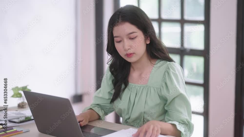 Young Asian woman using laptop computer technology typing lecture and studying online at home looking at screen sitting at desk, Distance Education Young Asian woman using laptop computer technology typing lecture and studying online at home looking at screen sitting at desk, Distance Education