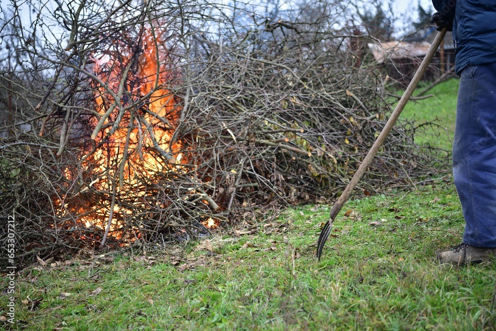 A gardener burns waste branches in a garden in a village traditionally