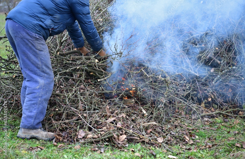 A gardener burns waste branches in a garden in a village traditionally