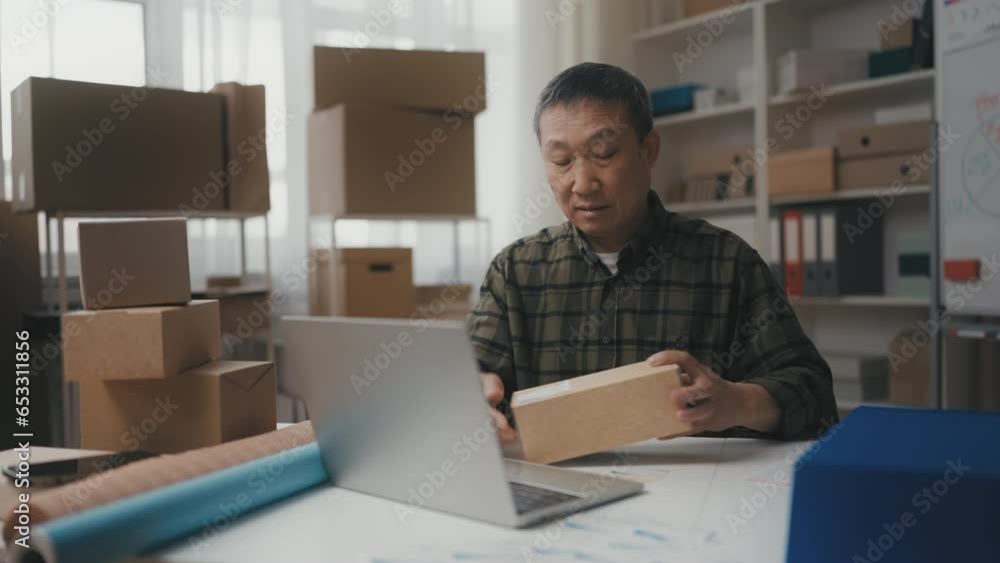 Senior Asian man entrepreneur packing orders for shipping, feeling overworked Senior Asian man entrepreneur packing orders for shipping, feeling overworked